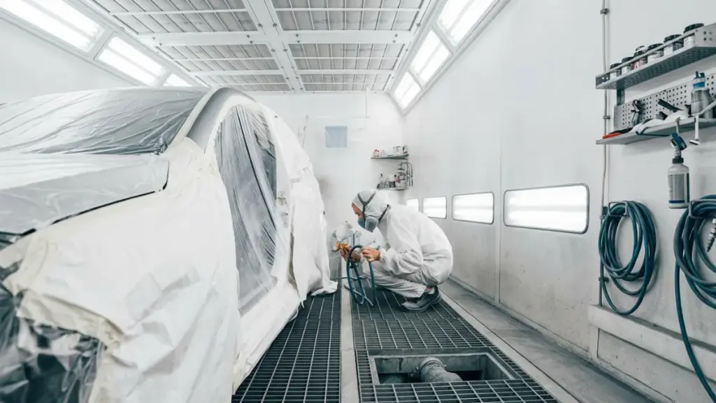 Technician spray painting car inside bright paint booth