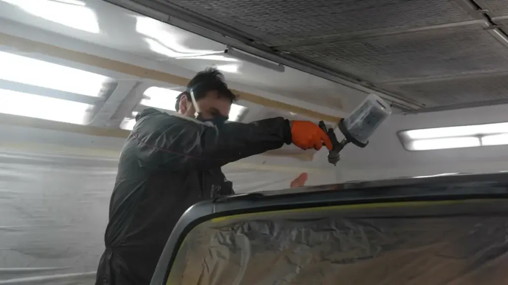 Worker spray painting car roof inside paint booth